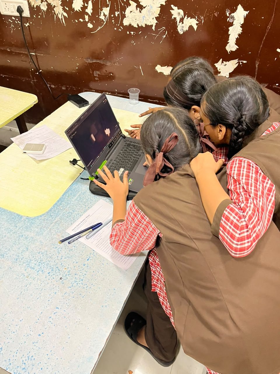 Three students huddle over a laptop, working on their game together