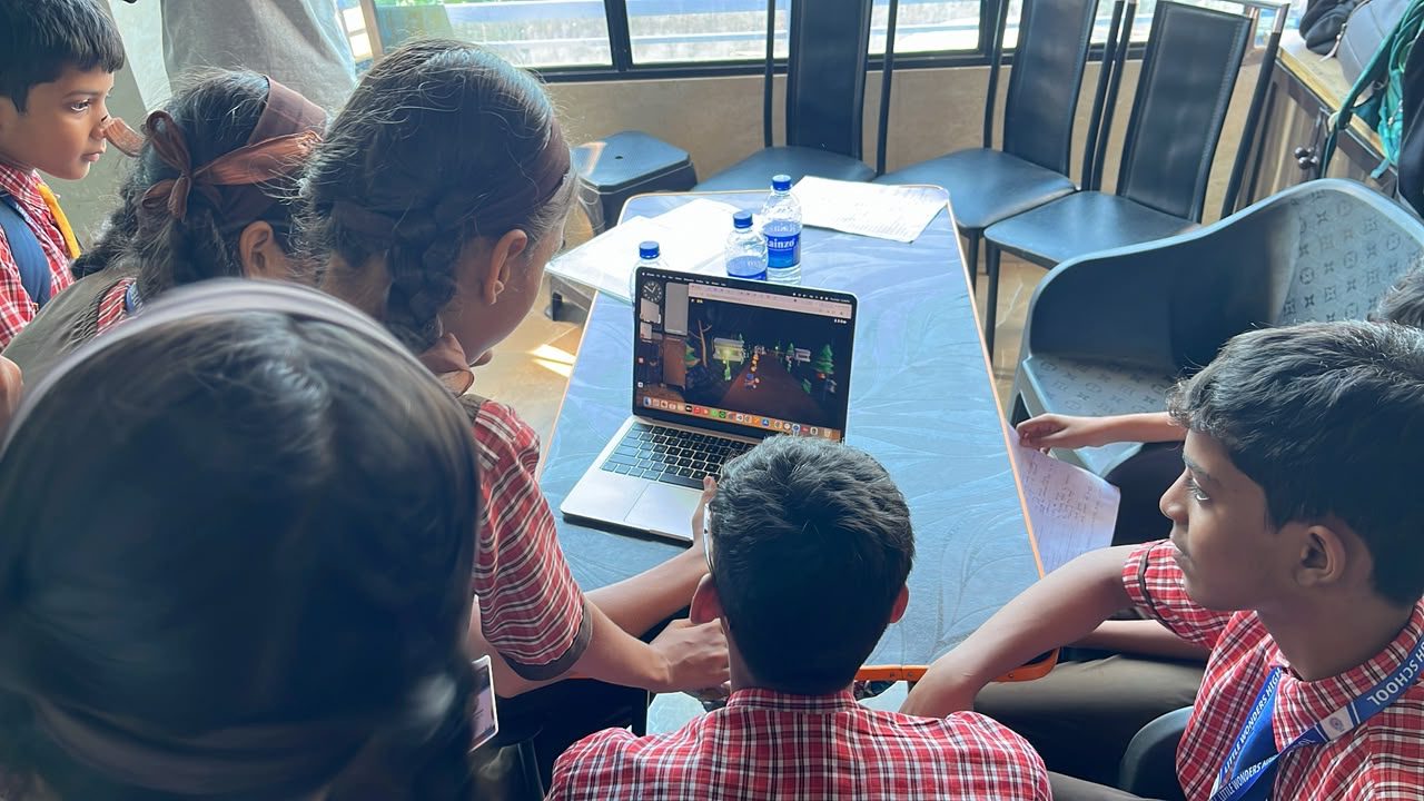 A group of students huddled around a laptop at a table, building a game together