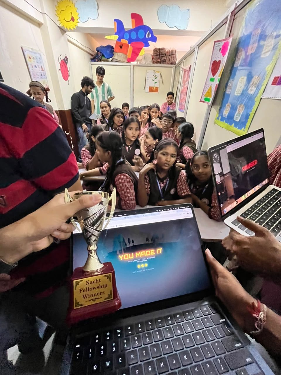 Students at a Nacht session gather around a laptop showing 'You made it', next to the Nacht Fellowship Winners trophy